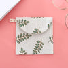 A light beige fabric pouch with a floral leaf pattern is shown against a pink background.