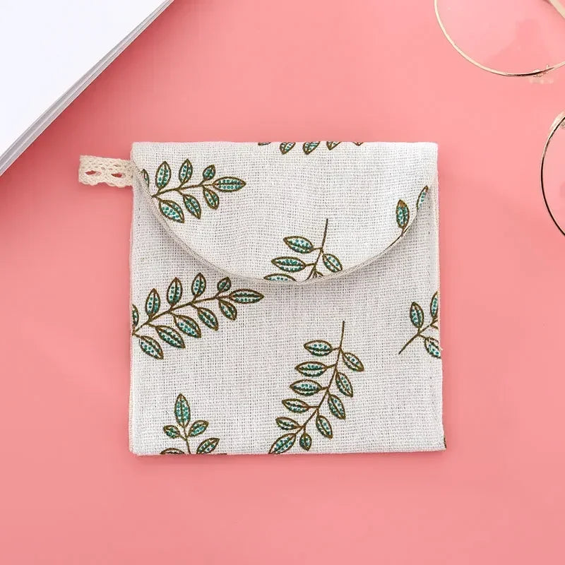 A light beige fabric pouch with a floral leaf pattern is shown against a pink background.