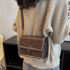 A brown leather mini cross-body bag with a gold chain is shown against a light beige knit sweater.