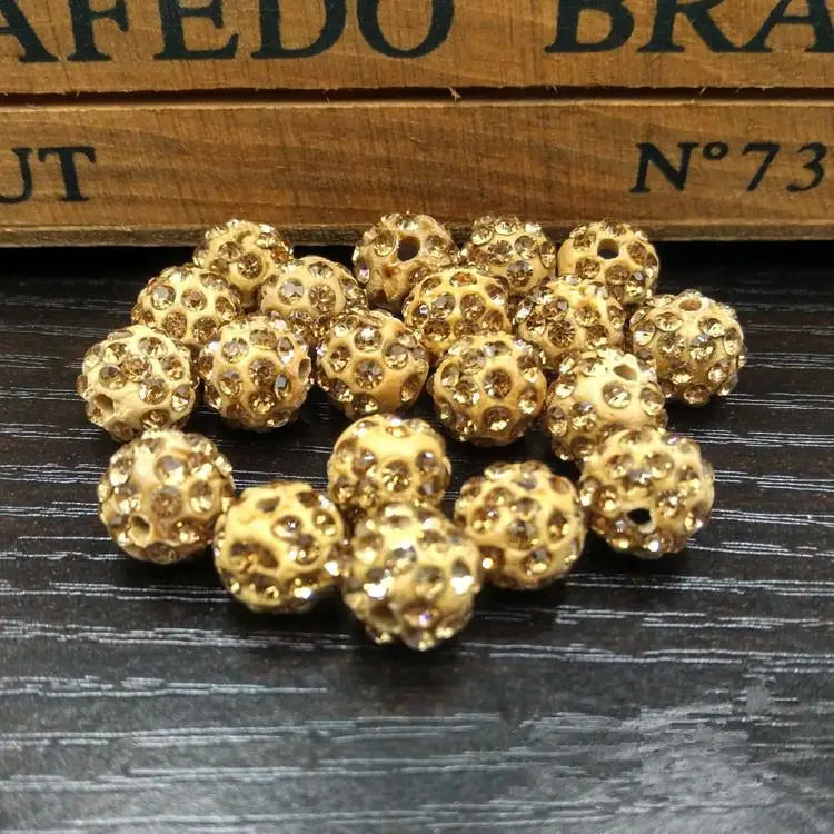 A pile of small, round, gold-colored crystal clay beads for jewelry making