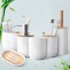 A set of white bamboo bathroom organizers and brushes with a soap dispenser on a light green background.