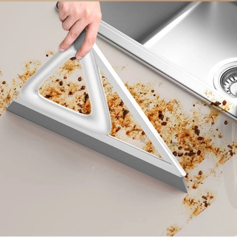 A hand is using a silicone squeegee broom to clean dried dirt from a surface.