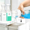 Three refillable laundry detergent dispenser bottles with labels are shown being filled into a clear bottle.