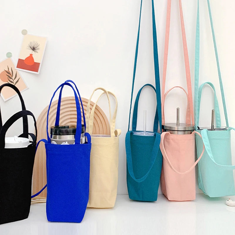 A collection of portable canvas water bottle crossbody bags in various shades of blue, pink, and mint green hanging on a whit