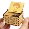 A wooden music box with a lid featuring a face design is held in a hand.