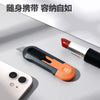 Un couteau utilitaire compact avec une poignée orange et une lame argentée à côté d'un smartphone.