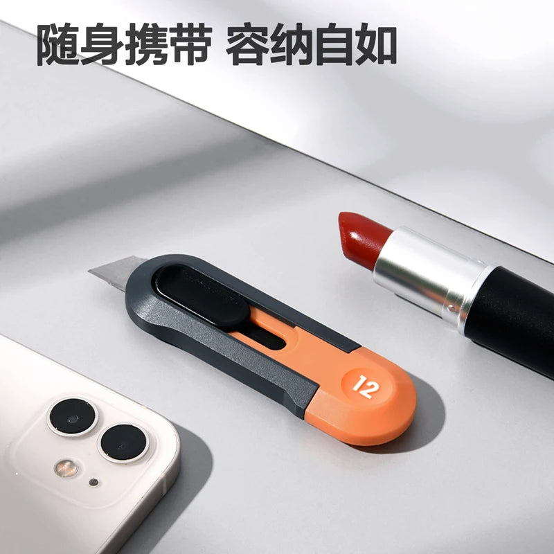 Un couteau utilitaire compact avec une poignée orange et une lame argentée à côté d'un smartphone.