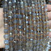 A hand holds a string of square faceted natural stone beads in various shades of blue and gray for jewelry making.