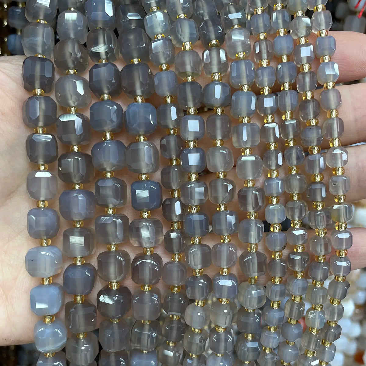 A hand holds a string of square faceted natural stone beads in various shades of blue and gray for jewelry making.