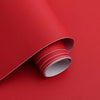 A roll of self-adhesive peel-and-stick wallpaper in a light gray color is shown partially unrolled against a vibrant red back