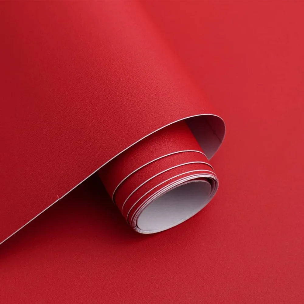 A roll of self-adhesive peel-and-stick wallpaper in a light gray color is shown partially unrolled against a vibrant red back