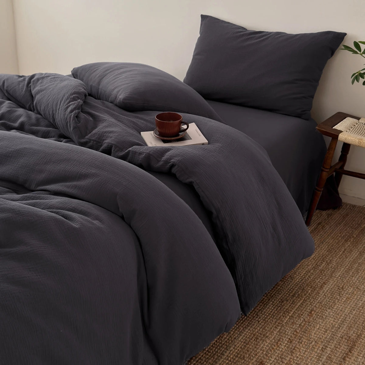 Dunkelgraue, faltige Bettwäsche-Set mit passenden Kissen und einer Tasse auf dem Bett.
