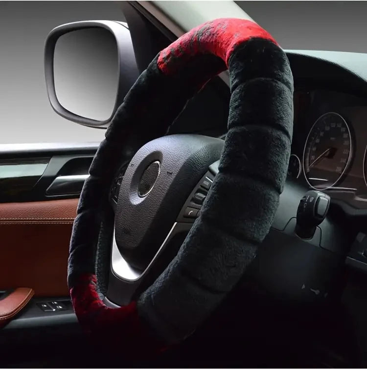 A close-up view of a black steering wheel covered with a red plush, fuzzy steering wheel cover.