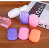 A collection of purple, pink, and orange portable disposable soap tablets next to a white bottle and packaging box.