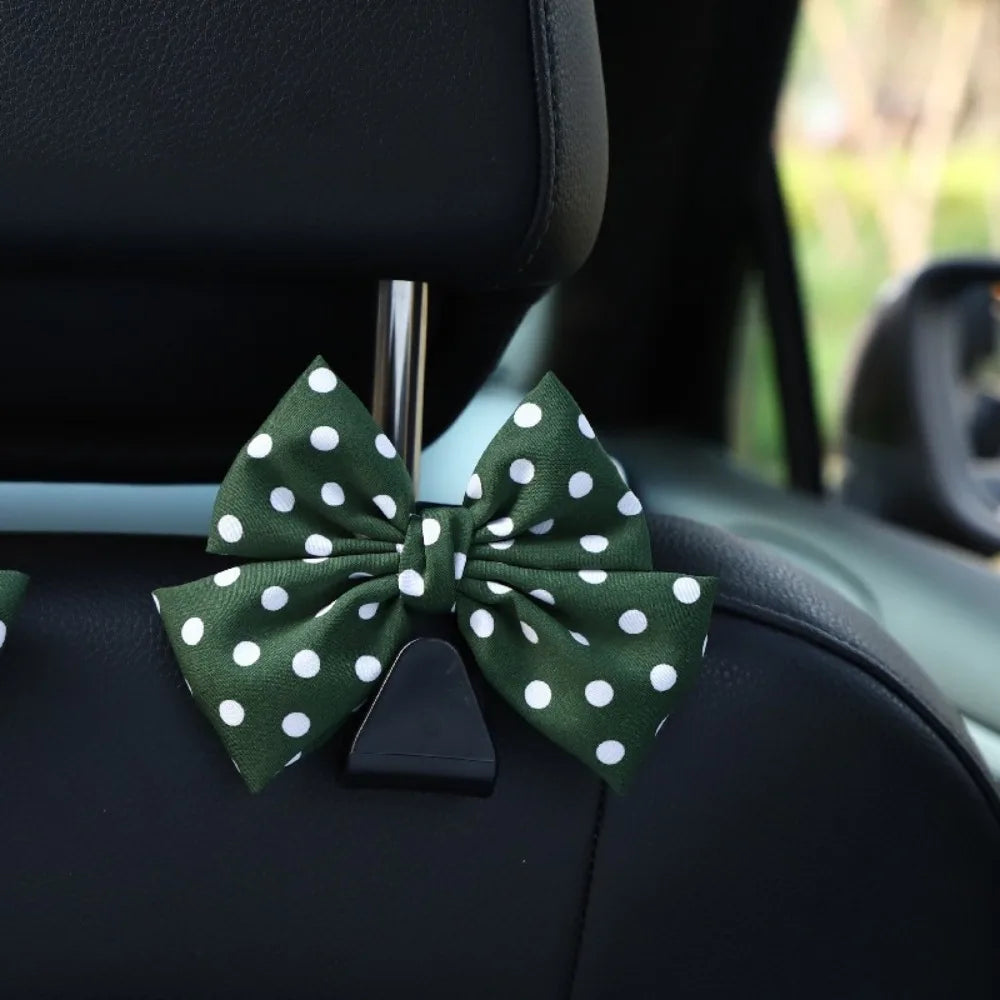 A dark green bow-shaped car seat back hook with storage attached to a black car seat.