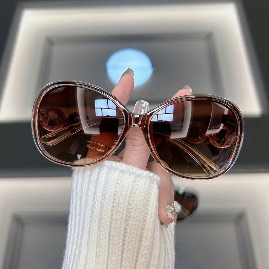 A hand holds a pair of brown vintage square sunglasses against a bright background.