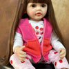 A lifelike 50 cm full silicone baby doll with long brown hair wearing a pink vest and pink pants.