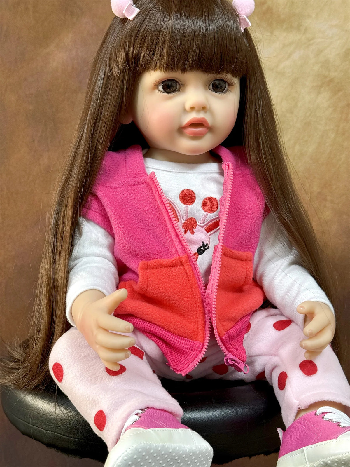 A lifelike 50 cm full silicone baby doll with long brown hair wearing a pink vest and pink pants.