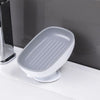 A white soap dish with a draining tray mounted on a white bathroom shelf.