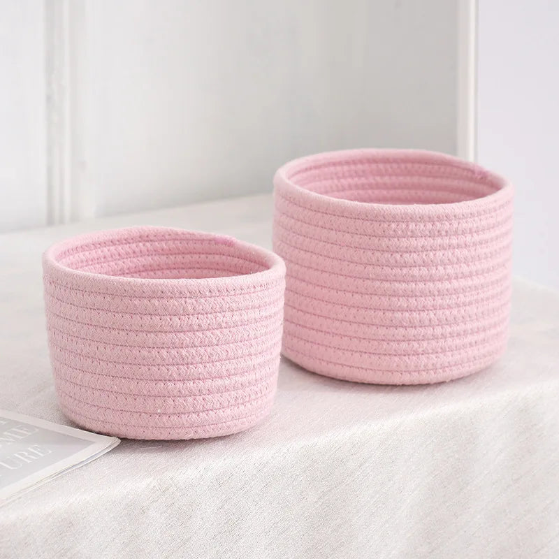 A pink handwoven cotton rope storage basket with a textured weave sits on a white surface.