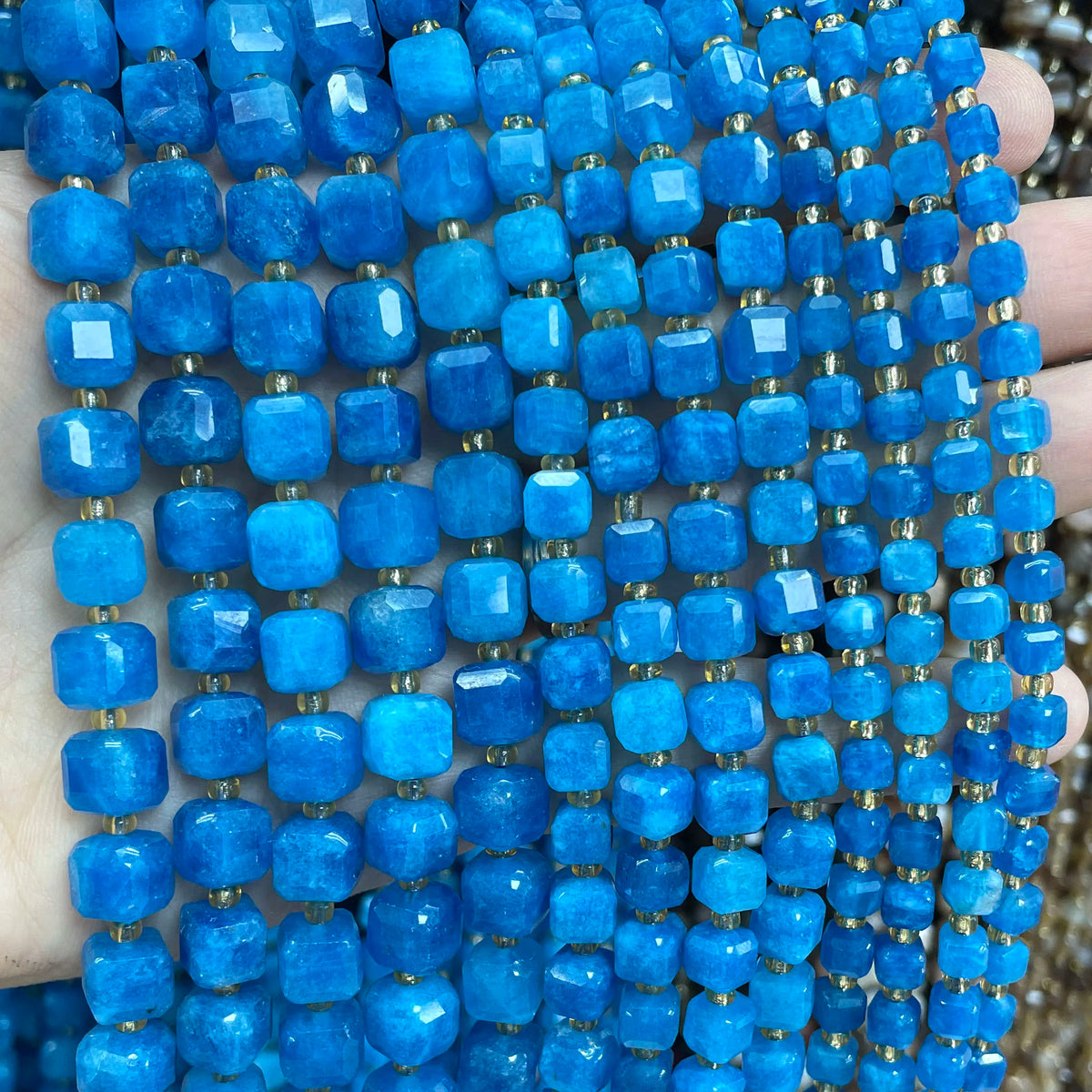 A hand holds a strand of bright blue natural stone square faceted beads for jewelry making.