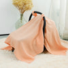 A peach colored breathable cotton muslin car seat and stroller cover lying on a white fluffy rug.