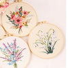 A collection of five round embroidery pieces featuring floral designs in soft pastel colors on cream fabric.