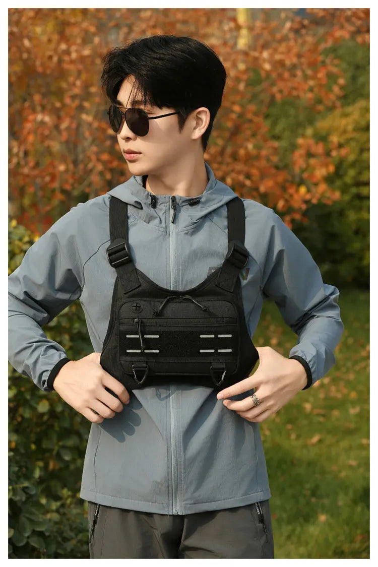 Junger Mann mit grauem taktischem Brustgurt, Laufvest und Sonnenbrille im Freien.