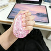 Eine Hand hält ein rosa glitzerndes Dumpling-Squishy-Stress-Relief-Spielzeug auf einem Tablet.