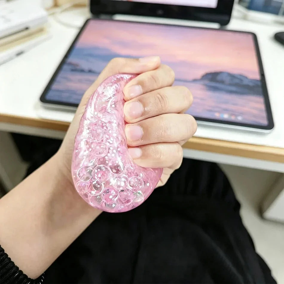 Eine Hand hält ein rosa glitzerndes Dumpling-Squishy-Stress-Relief-Spielzeug auf einem Tablet.