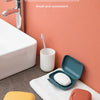 A small, leak-proof travel soap box in orange and yellow sits on a white towel next to a sink.