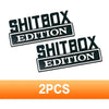 Zwei schwarze rechteckige Aufkleber mit der Aufschrift SHITBOX EDITION auf weißem Hintergrund.
