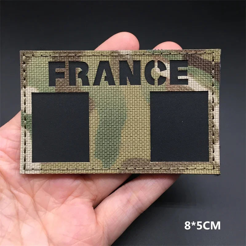 A close-up of a fabric tactical patch featuring the word FRANCE in large letters on a camouflage background.