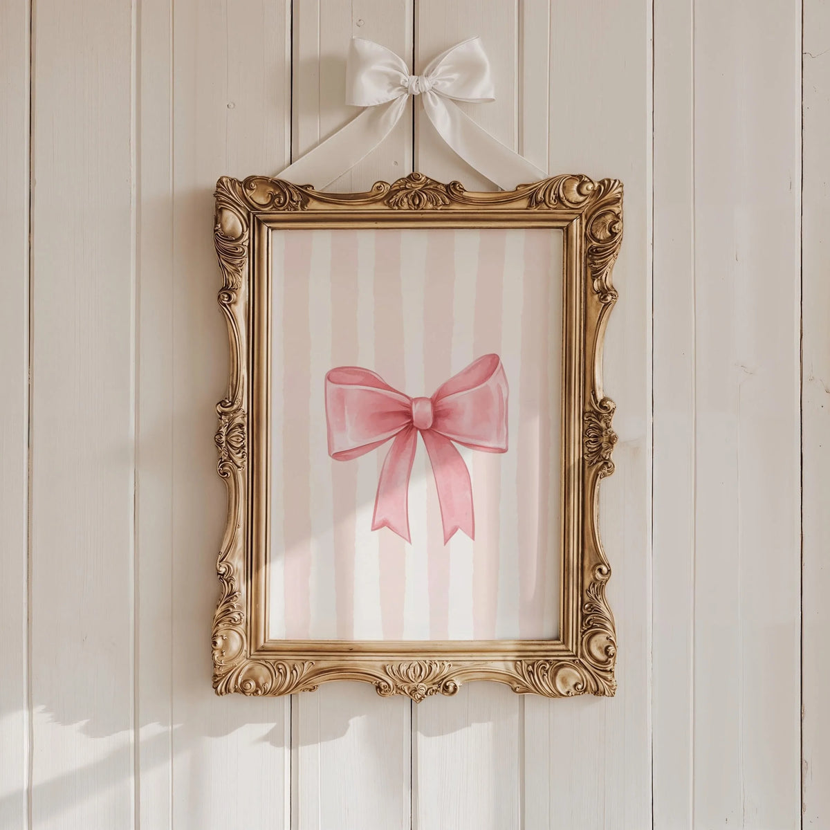 A framed canvas print featuring pink and white vertical stripes and a pink bow on a light wood wall.