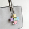 A silver keychain featuring a cross shape made of colorful, translucent silicone fidget cubes attached to a light gray leathe