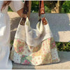 Sac à l'épaule patchwork blanc et floral avec un haut en maille et des sangles en cuir marron, exposé à l'extérieur.