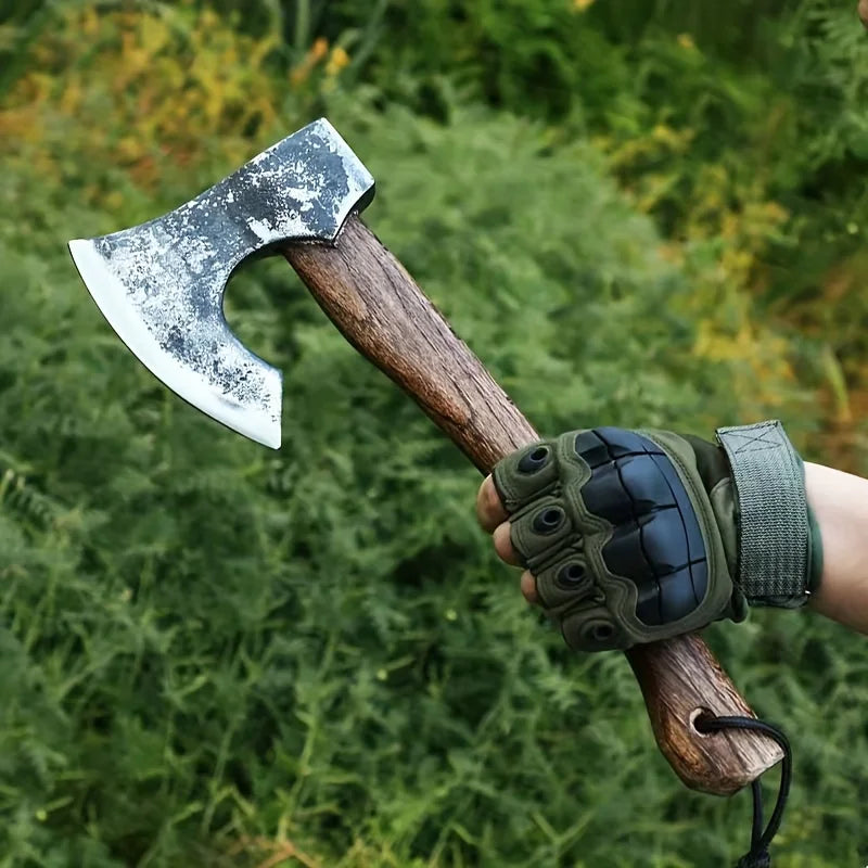 A hand-forged Viking tomahawk axe with a wooden handle and dark green leather grip is held in a natural outdoor setting.