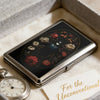 A vintage metal card and cash case with an art deco design featuring a dark floral pattern set in a square box.