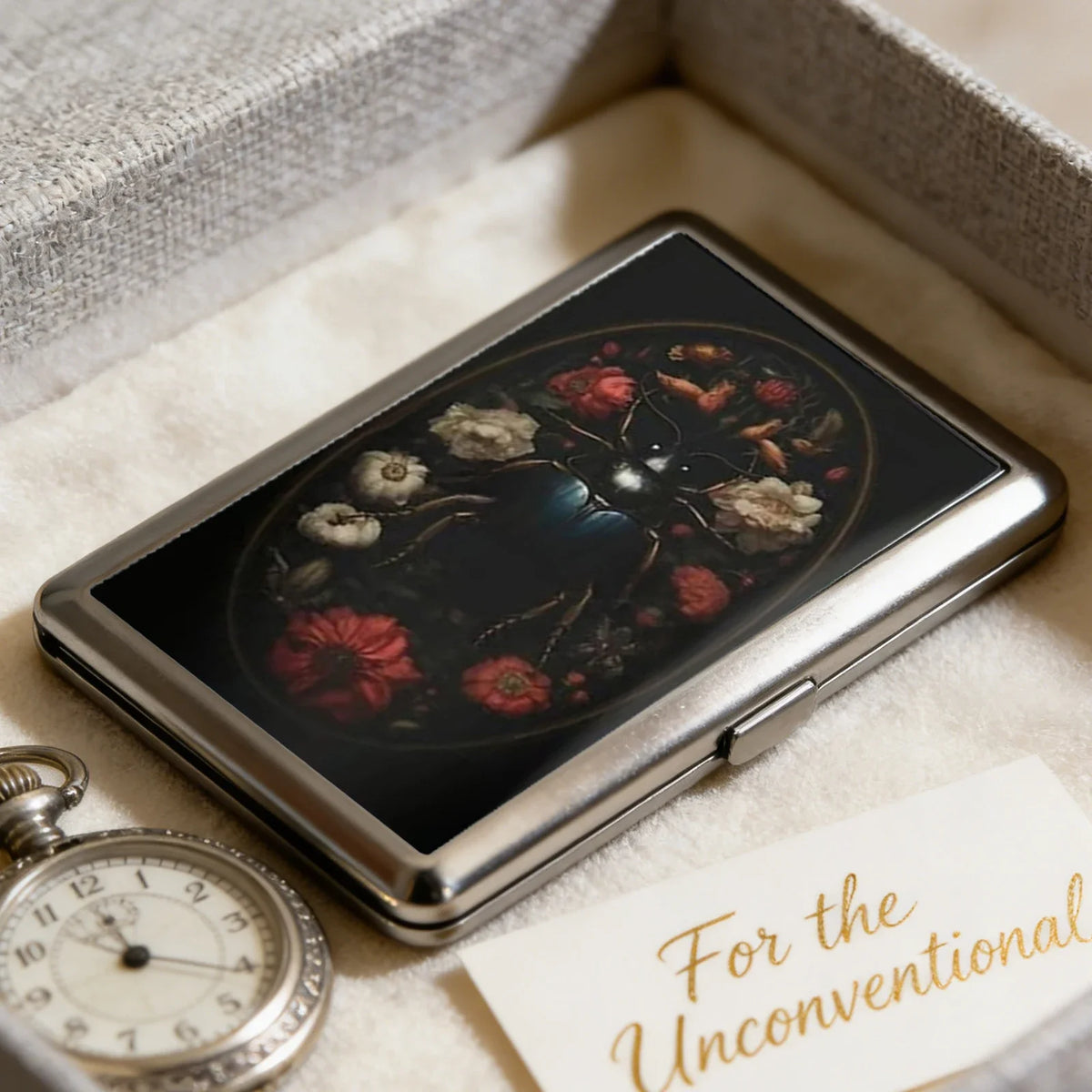 A vintage metal card and cash case with an art deco design featuring a dark floral pattern set in a square box.