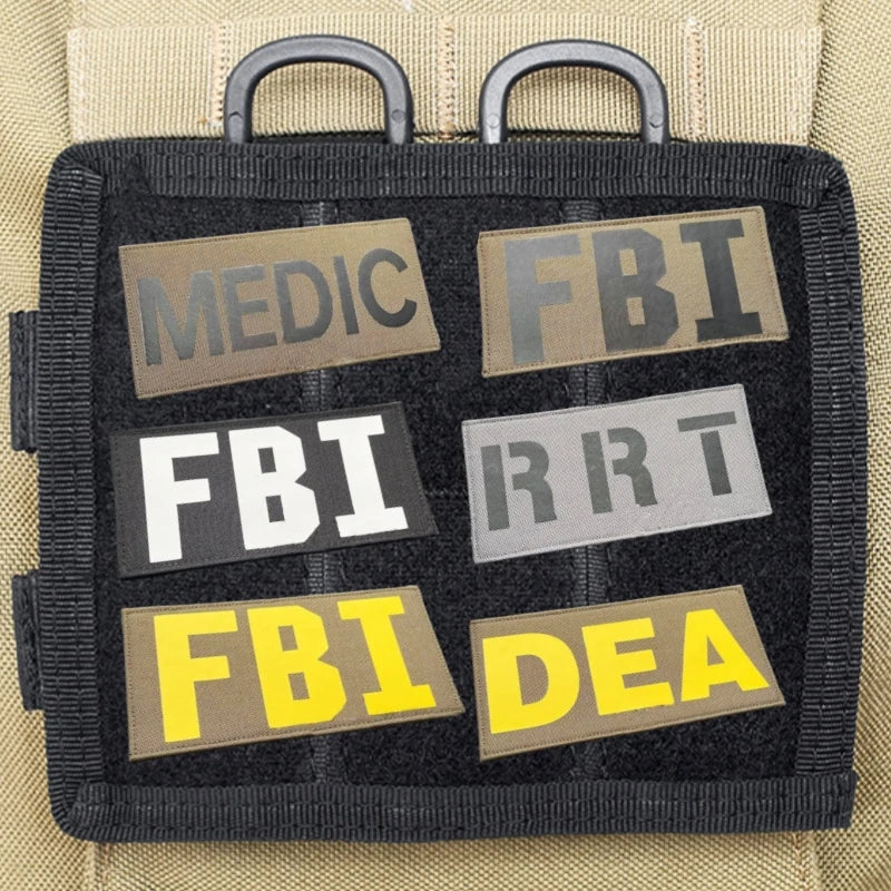 A black tactical patch with embroidered labels for MEDIC, FBI, RRT, and DEA on a beige fabric background.