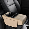 A beige car armrest cushion with a black cupholder and storage compartment is placed on a dark leather seat.