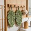 A green banana leaf absorbent hand towel is hanging on a wooden rack.
