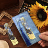 A vintage metal bookmark with an artistic hollow design and tassel is shown next to a sunflower on a wooden surface.