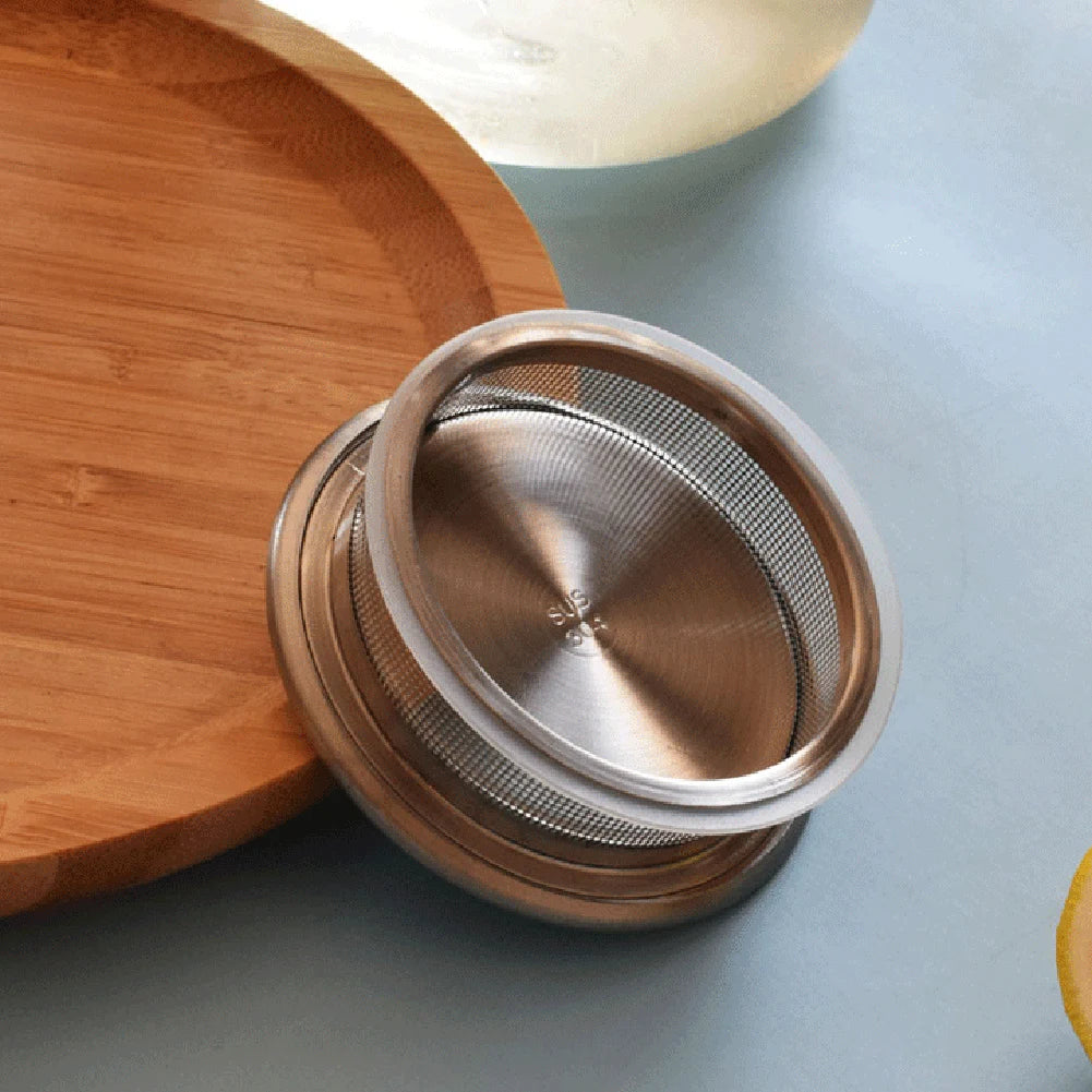 A stainless steel filter is shown resting on a wooden plate against a light blue background.