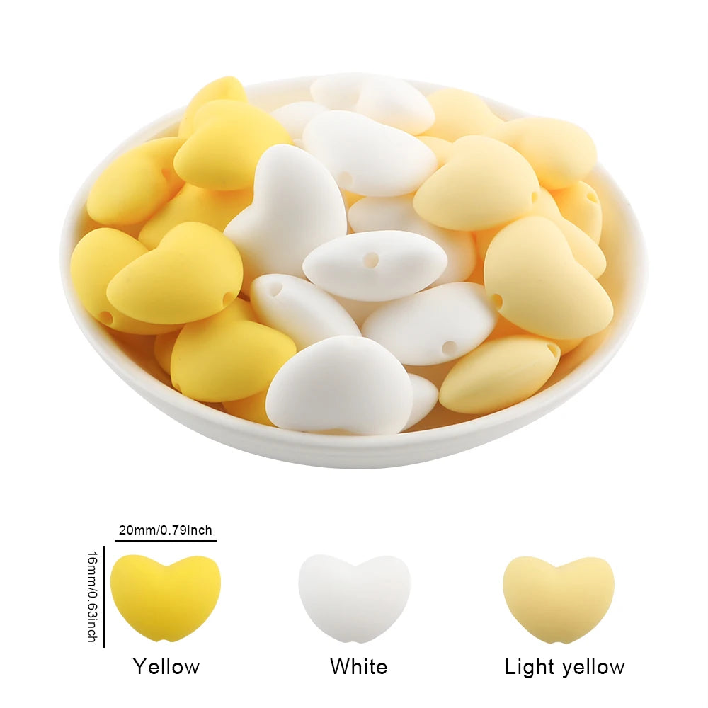 A bowl filled with ten silicone heart beads in yellow, white, and light yellow colors.