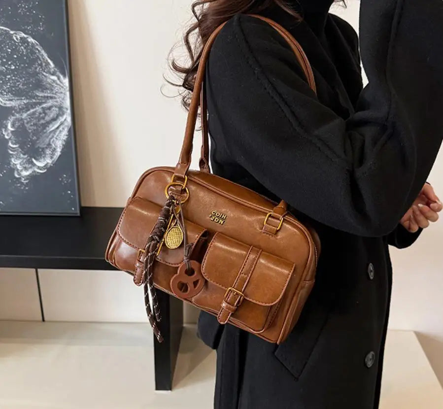 A woman holds a brown leather multi-pocket shoulder handbag against a dark background.