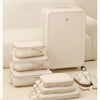 A set of white compressible packing cubes stacked and displayed on a light rug next to a large white suitcase.