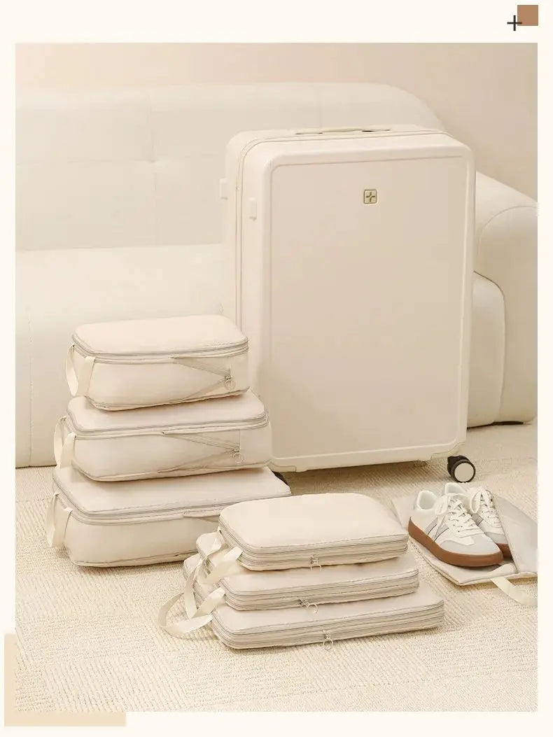 A set of white compressible packing cubes stacked and displayed on a light rug next to a large white suitcase.