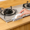 A hand is cleaning a stovetop burner using a white groove cleaning brush with a replaceable scouring head.