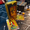 A gold foil tarot card deck box and several cards are displayed on a dark surface.